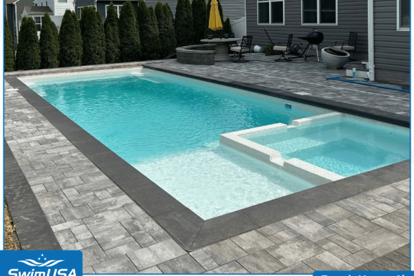 Backyard swimming pool with stone deck and attached spa beside a modern house