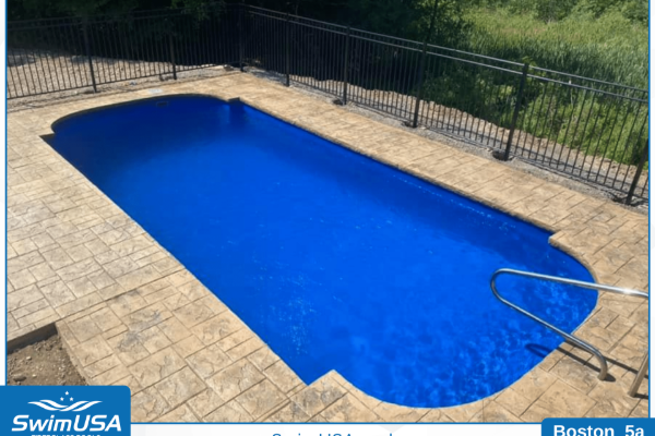 Empty rectangular in-ground pool with blue water, tan pavers, and black metal fence.