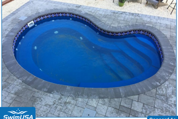 Blue kidney-shaped swimming pool with curved steps, surrounded by light gray stone patio.