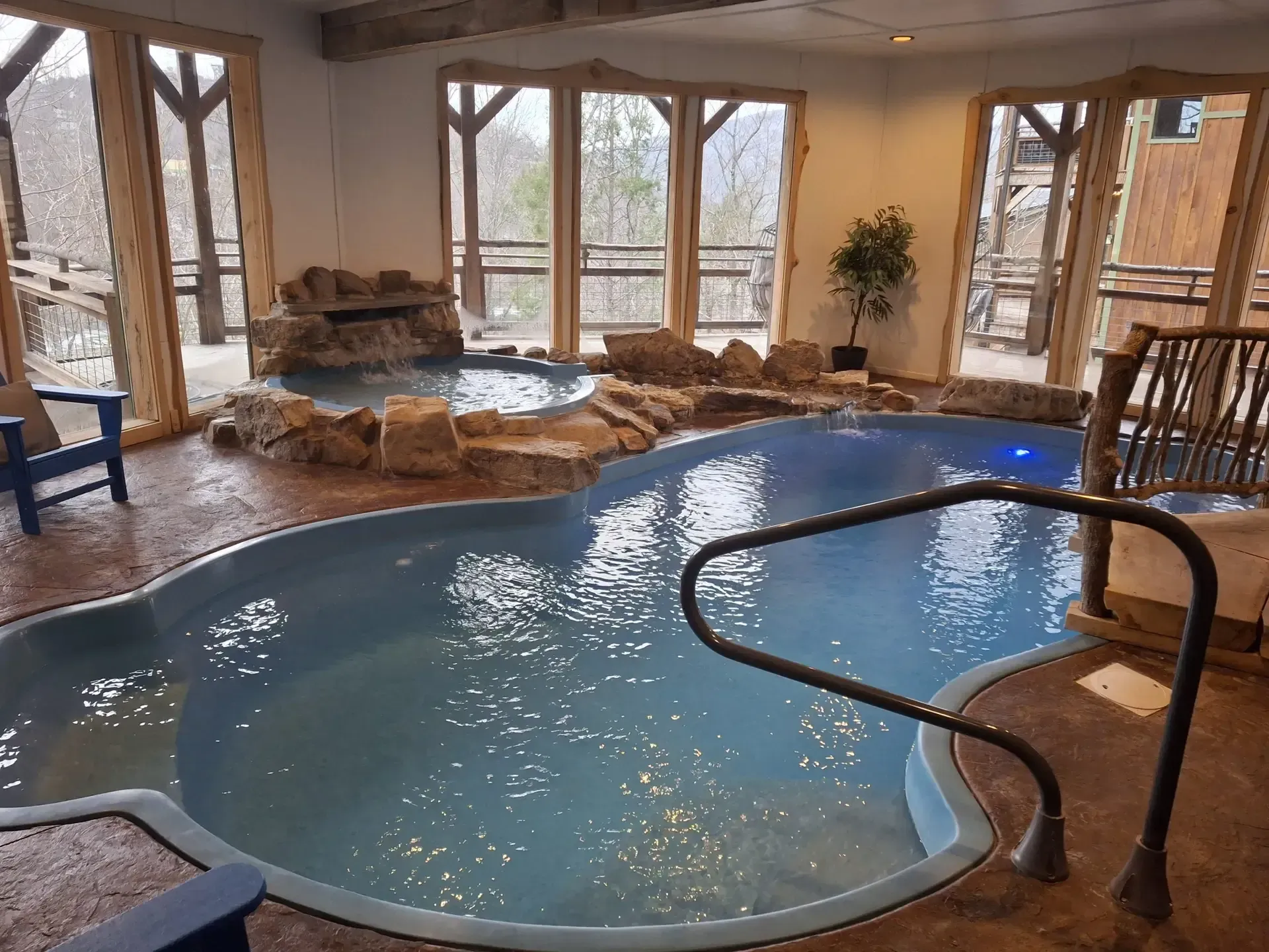 Indoor pool with rock waterfall, blue water, and large windows in a bright spa-like room