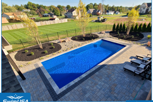 Backyard with a rectangular blue in-ground pool, paved patio, and lounge chairs overlooking a lawn
