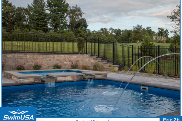Backyard pool with blue water, stone steps, and a black fence overlooking a green lawn.