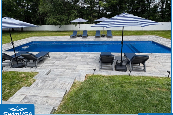 Backyard swimming pool with stone patio, lounge chairs, striped umbrellas, and green lawn