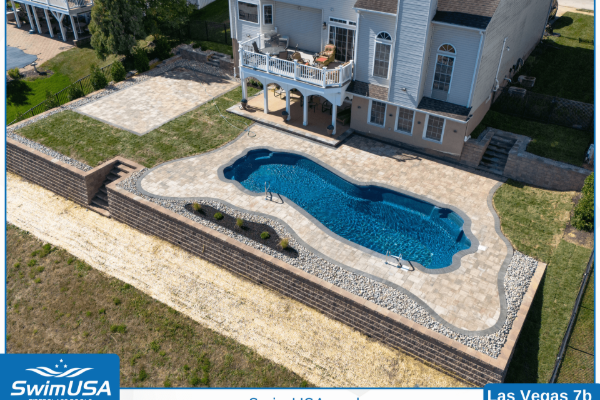 Elevated backyard pool with blue water, stone deck, and house patio stairs behind it