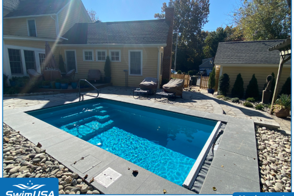 Backyard pool with blue water, stone deck, lounge chairs, and a house in the background