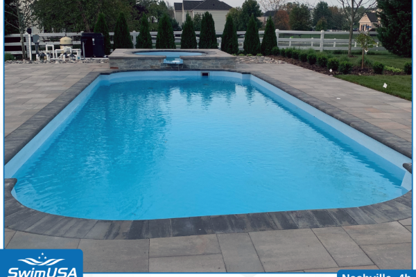 Rectangular outdoor swimming pool with bright blue water, stone deck, and hedges in the background