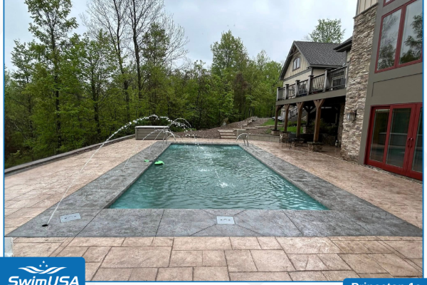 Rectangular backyard swimming pool with stone deck beside a house and wooded trees