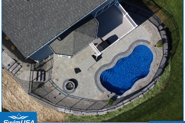 Aerial view of a backyard with a kidney-shaped blue swimming pool and patio beside a house