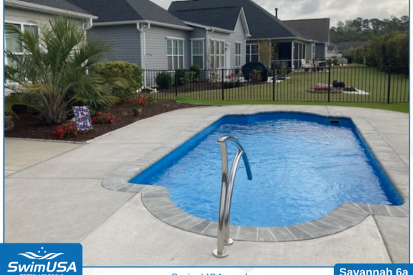 Backyard swimming pool with blue water, paved deck, and metal handrail beside a house