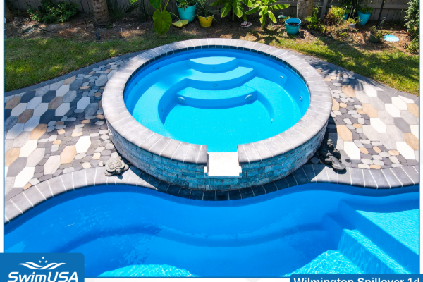 Backyard pool with circular spa and blue water, bordered by gray stone pavers and greenery