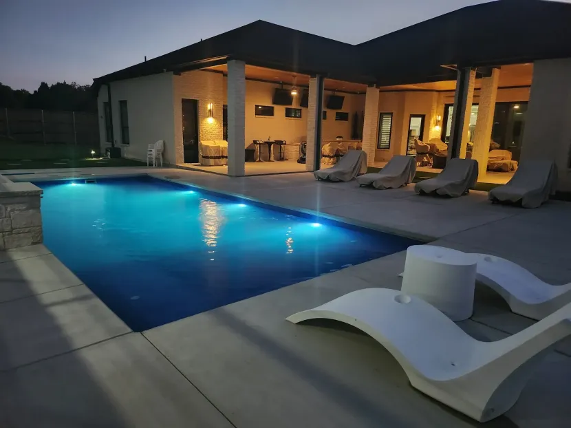 Modern villa with glowing blue pool and lounge chairs at dusk