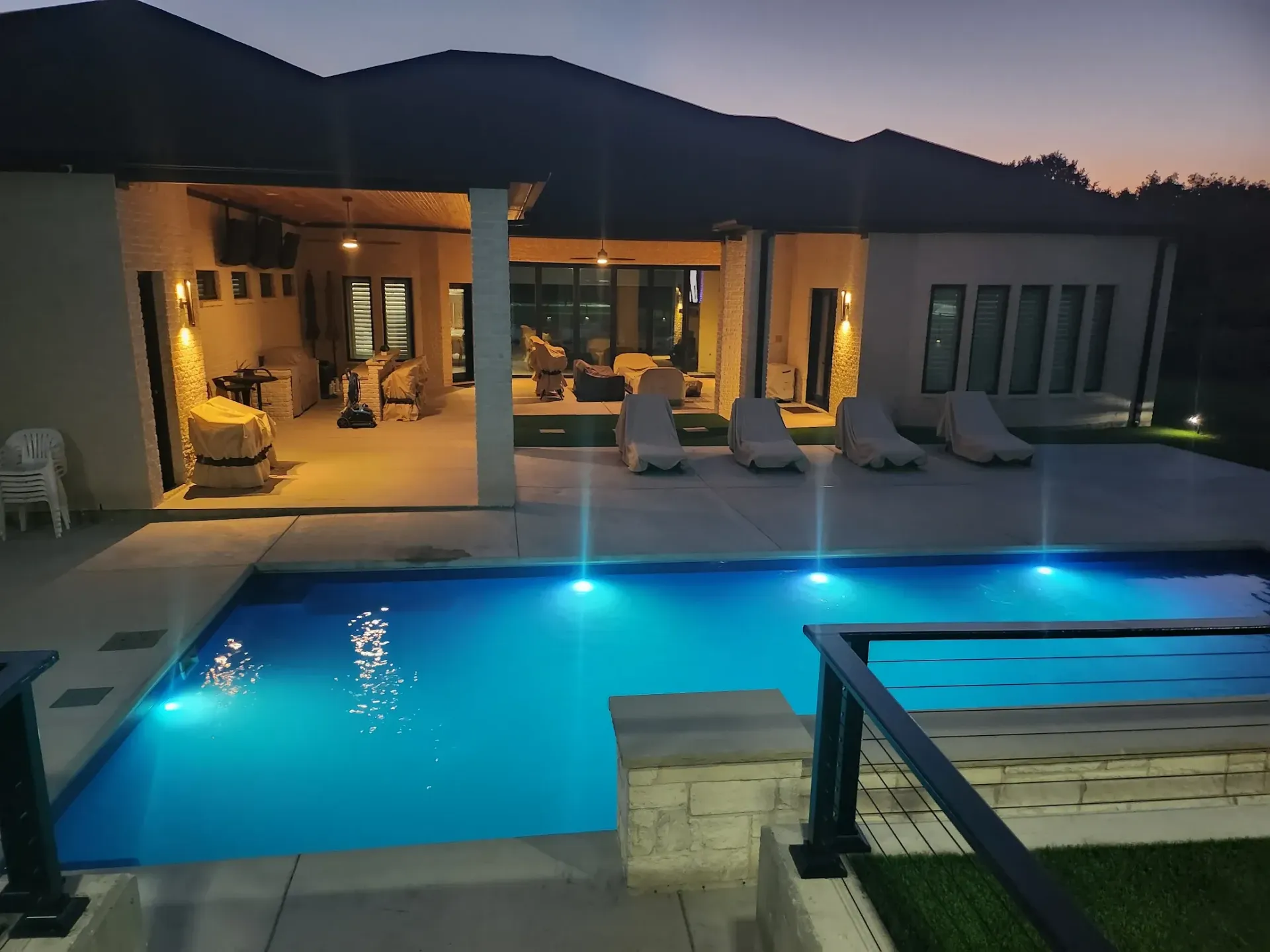 Modern villa patio with a lit blue swimming pool at dusk and outdoor lounge seating