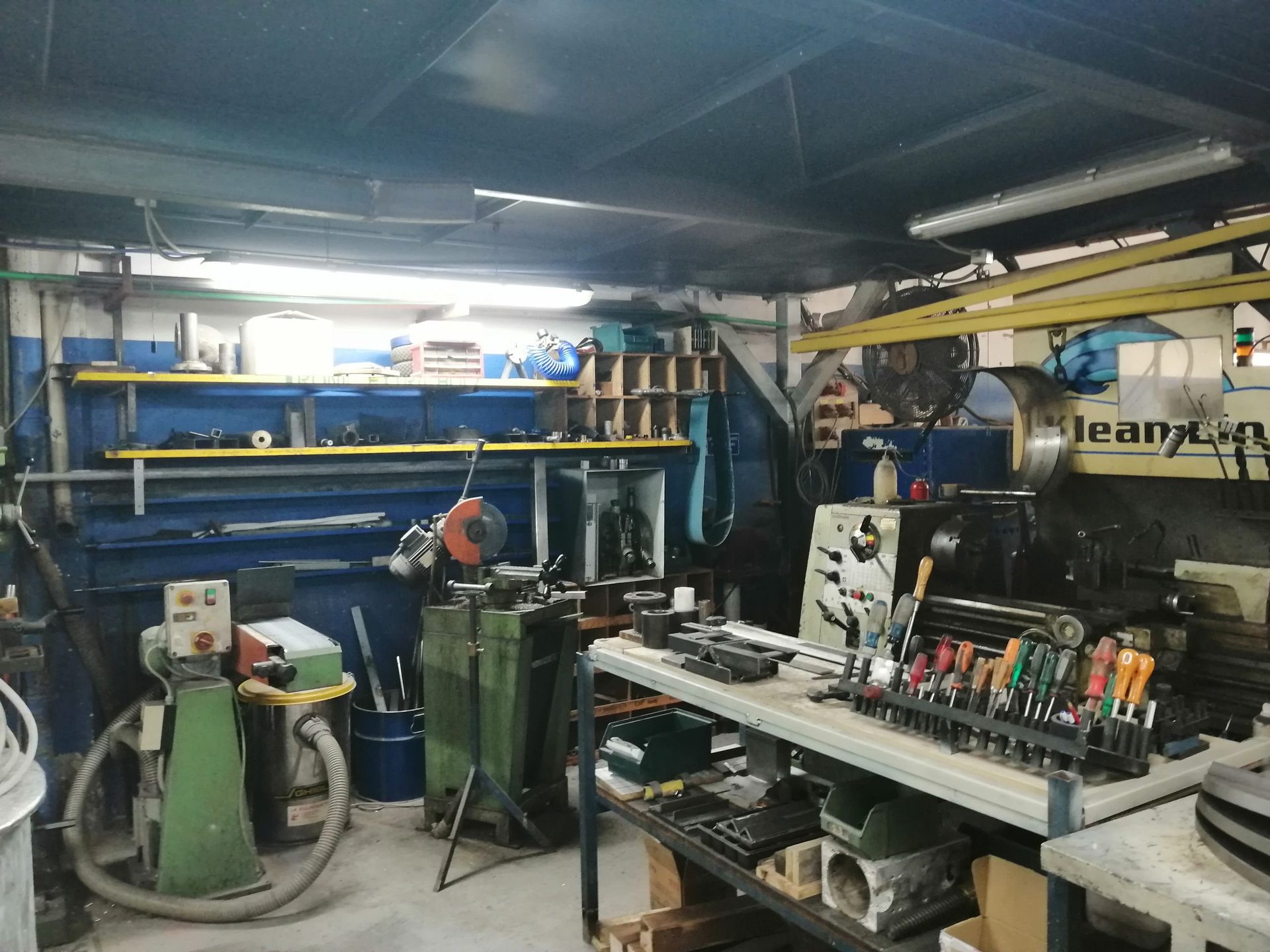 Interno dell'officina, utensili e attrezzature visibili. Scaffali, metallo e macchinari vari.