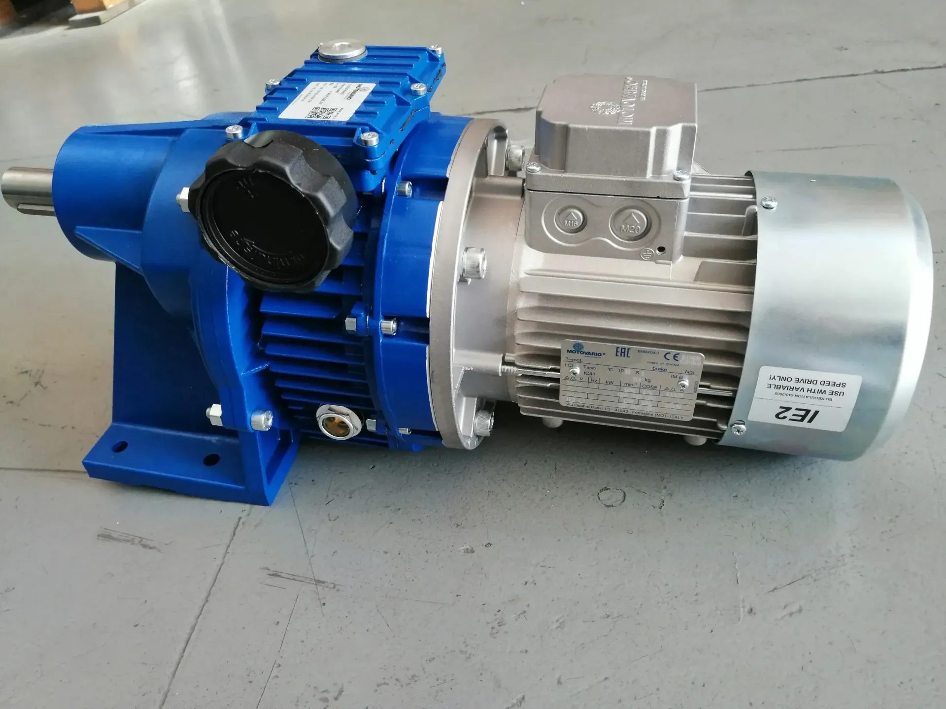 Motore elettrico blu e argento con riduttore su superficie grigia.