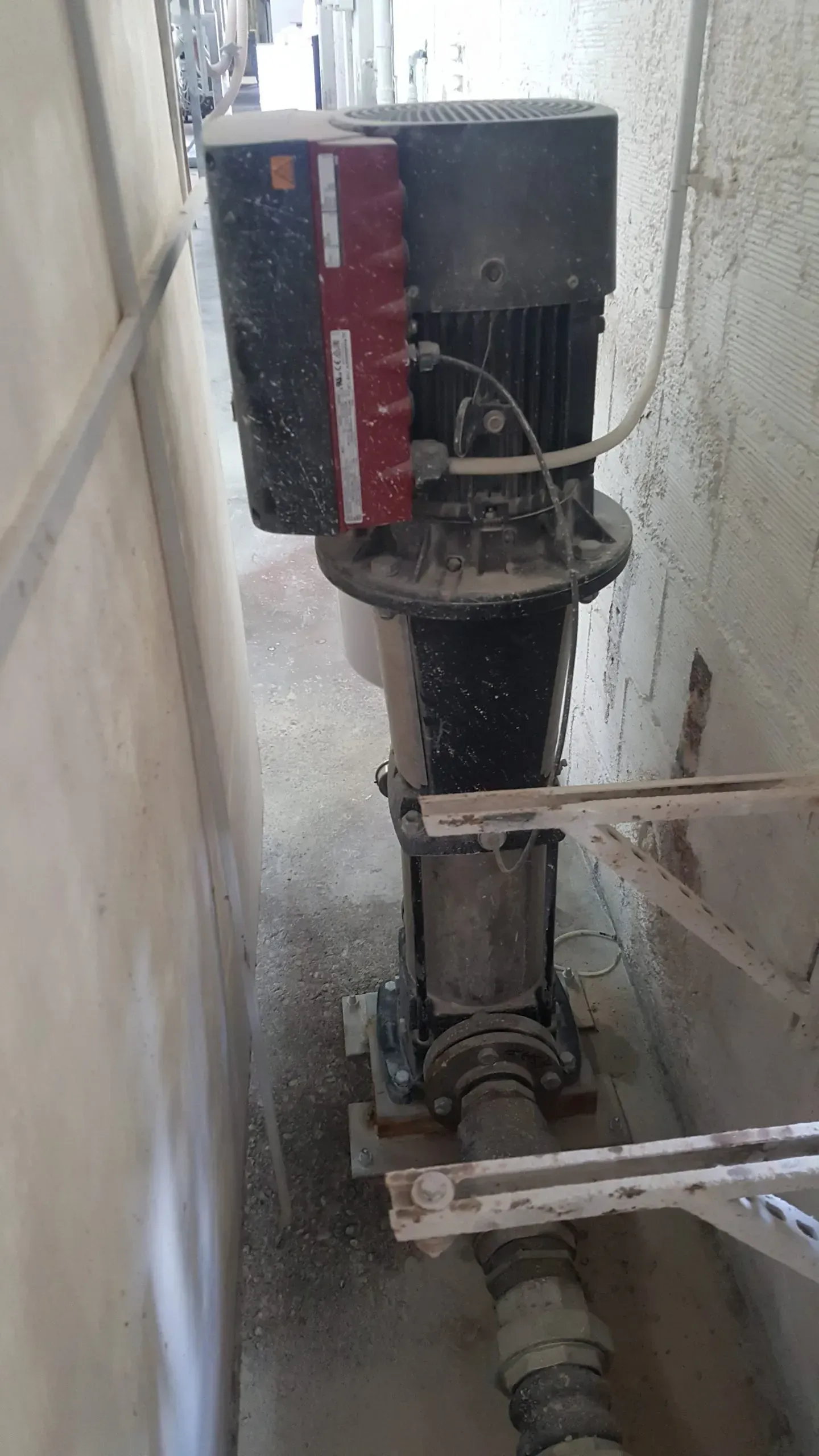 Pompa verticale con motore nero e pannello rosso, in un ambiente industriale.