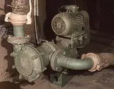 Pompa industriale verde con motore, tubi e flange in un ambiente poco illuminato.