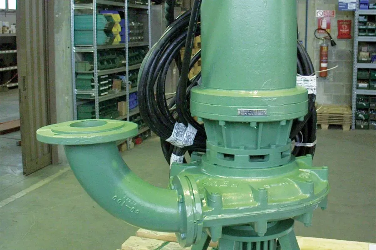 Pompa industriale verde con tubo curvo e cavi collegati in un magazzino.