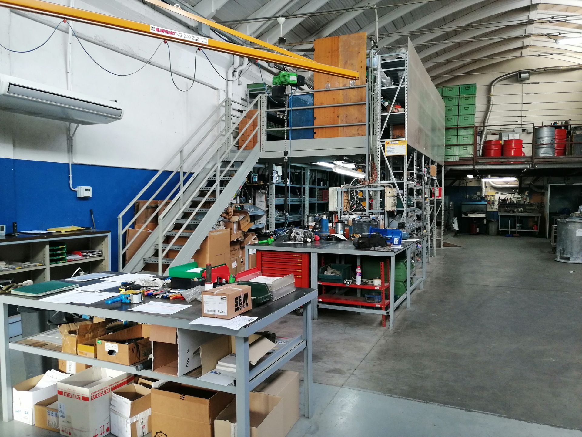 Interno dell'officina con scaffalature metalliche, banchi da lavoro e scale che conducono a un soppalco.