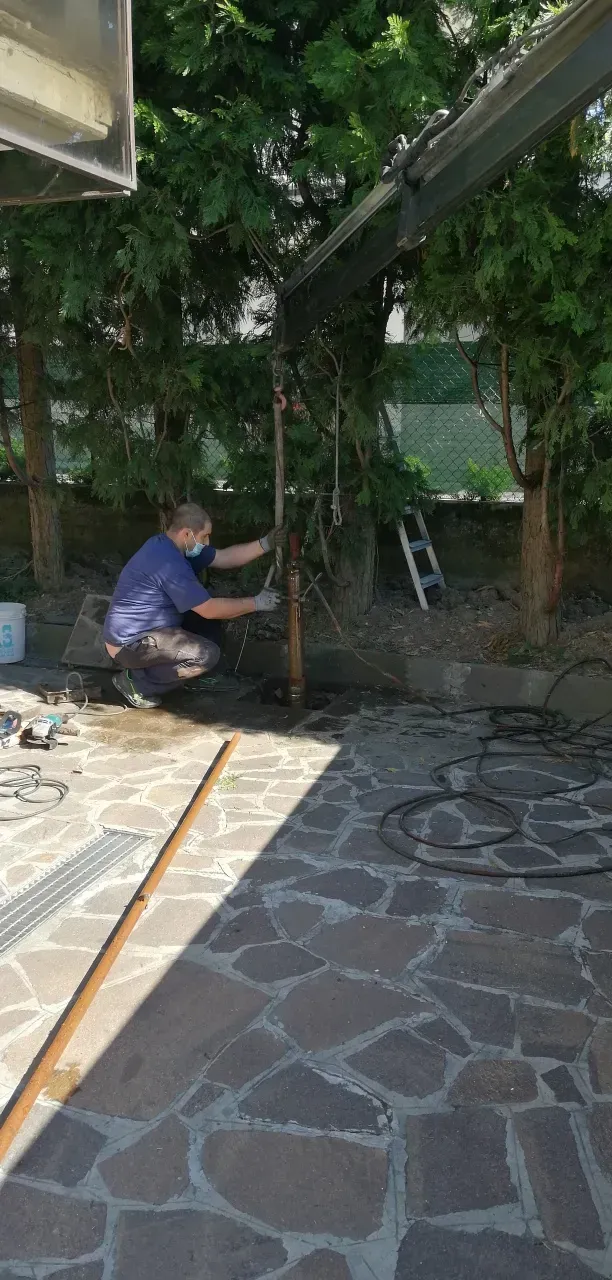 Una persona lavora su una struttura di supporto in metallo in un cortile con patio in pietra. Alberi sullo sfondo.