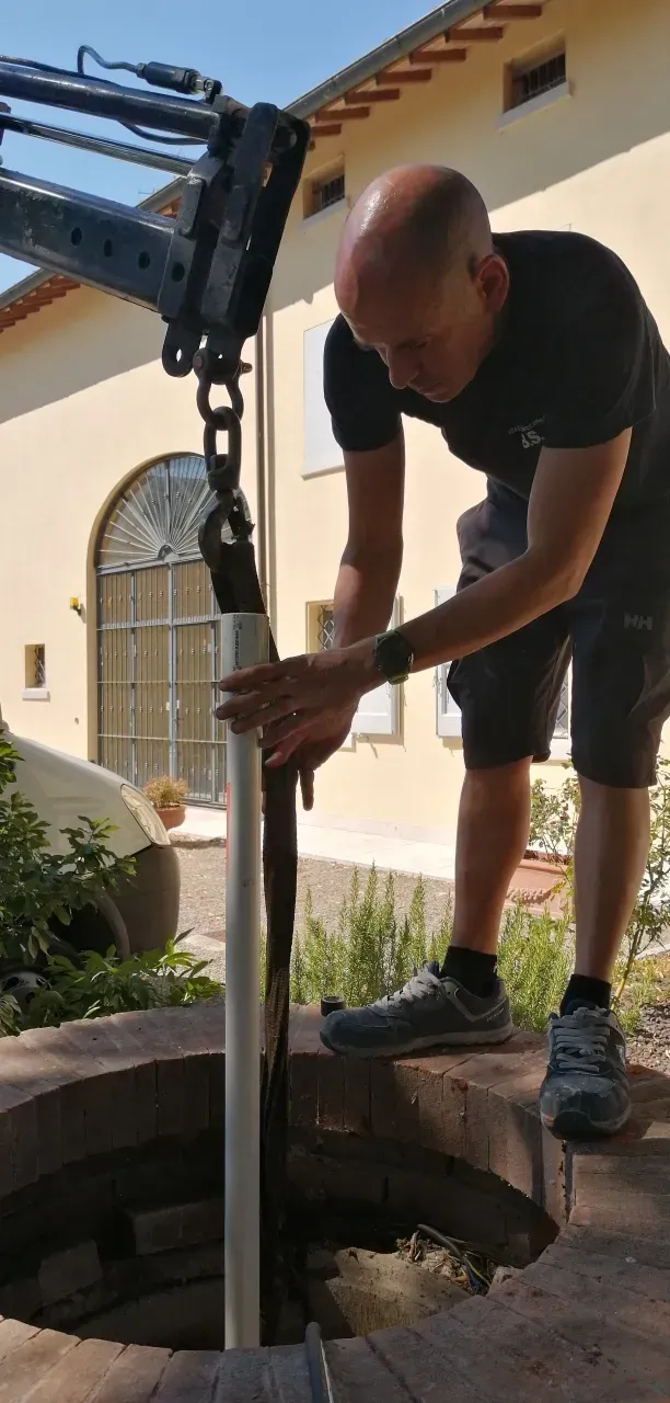 Uomo che installa un tubo nell'apertura di un pozzo, con l'ausilio di macchinari, all'aperto, vicino a un edificio.