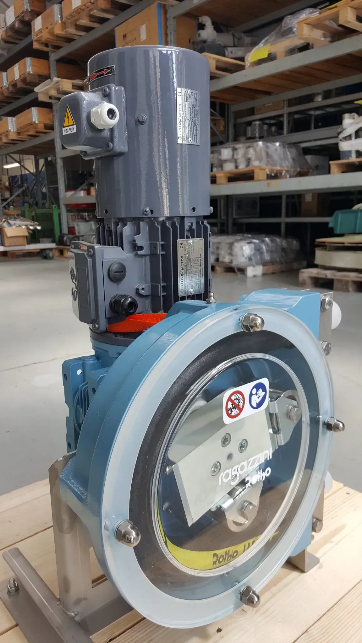 Pompa industriale blu e grigia con motore elettrico, coperchio trasparente, su supporto in legno.