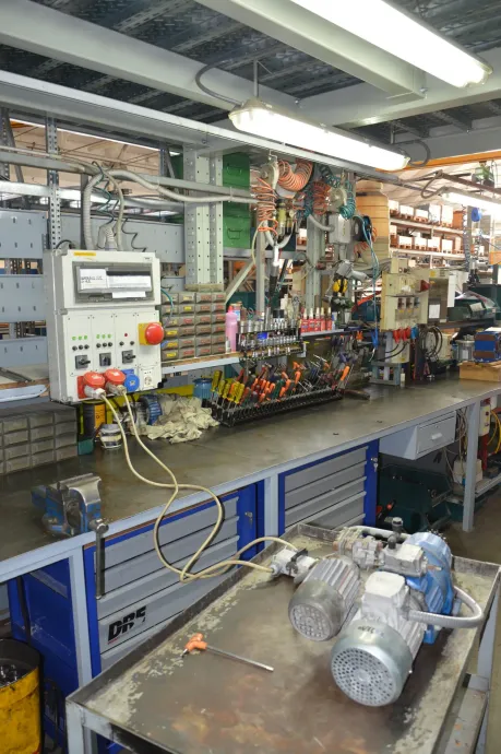 Officina con banco da lavoro, attrezzatura e pannello di controllo. Contiene un motore e utensili.