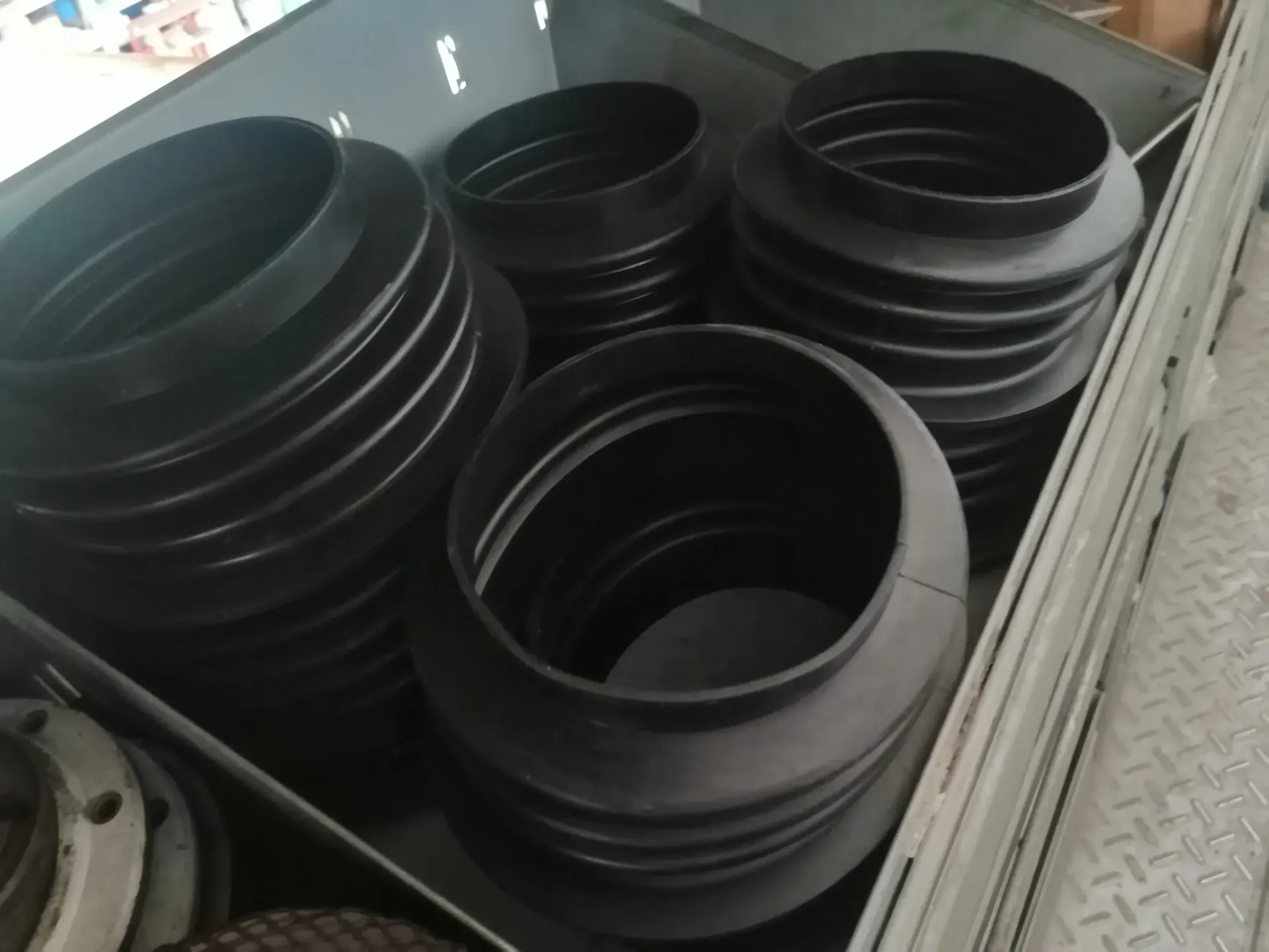 Soffietti in gomma nera, impilati all'interno di un contenitore metallico, per uso industriale.