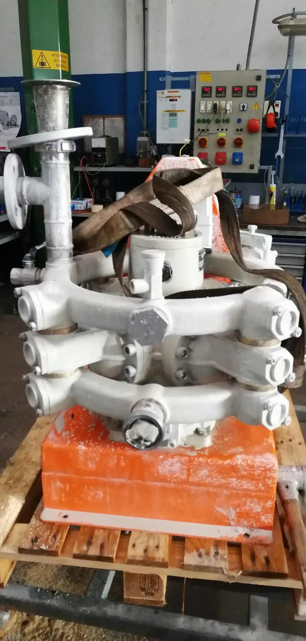 Attrezzatura industriale bianca fissata con una cinghia su un blocco arancione e un pallet di legno, all'interno.