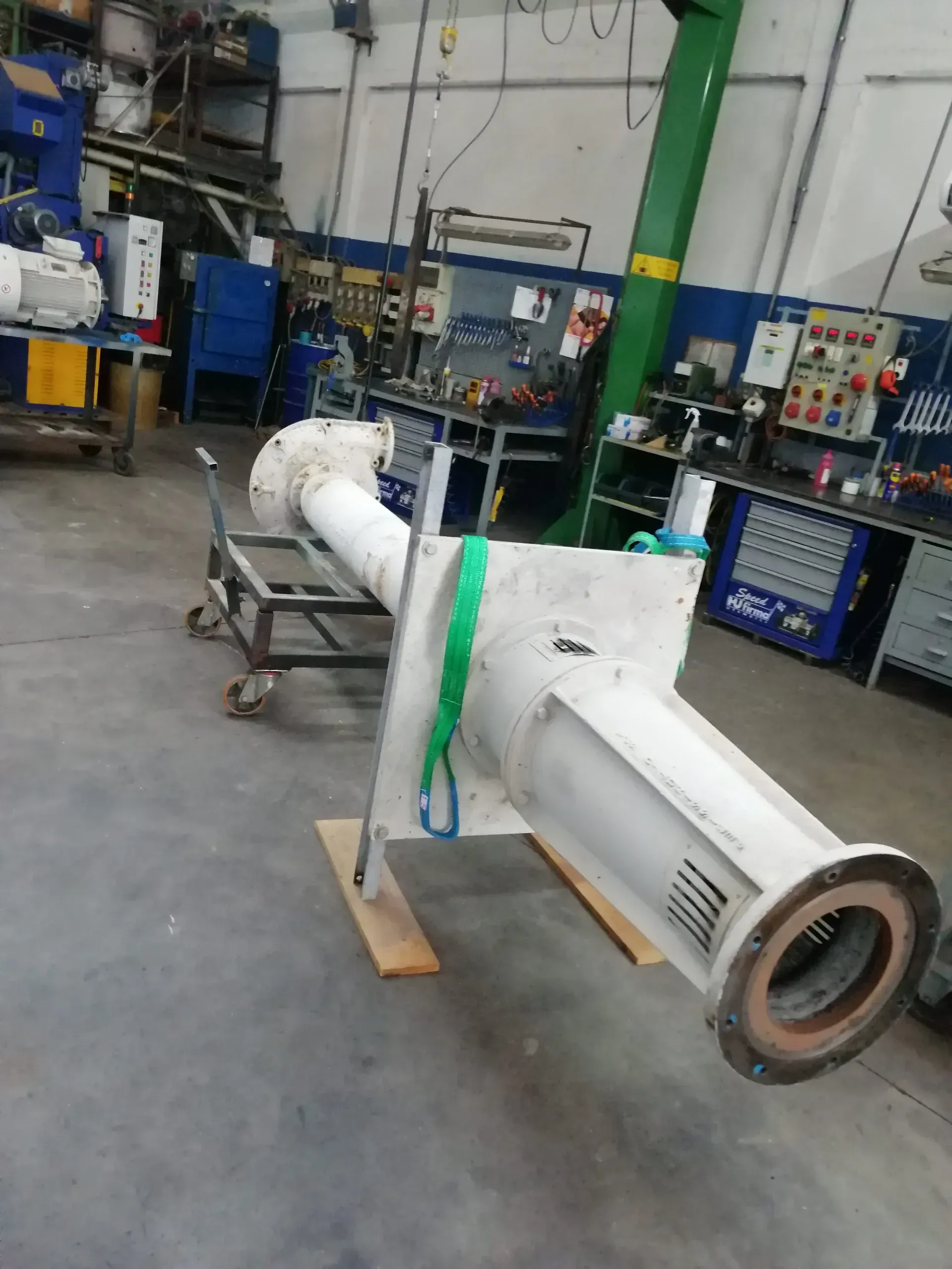 Grande pompa industriale bianca sul pavimento di un'officina, fissata con una cinghia verde.