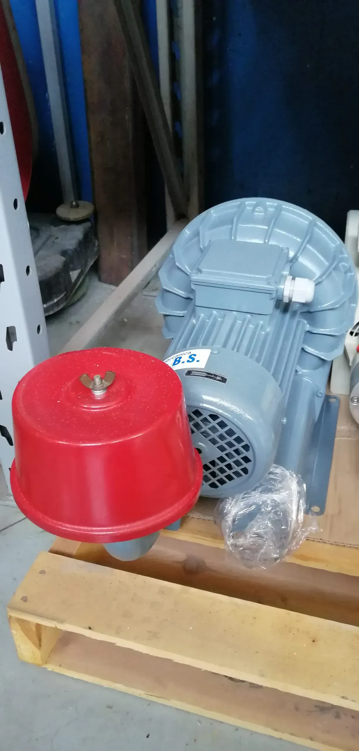 Una pompa dell'aria grigia e un filtro dell'aria rosso sono posizionati su un pallet di legno in un'officina.