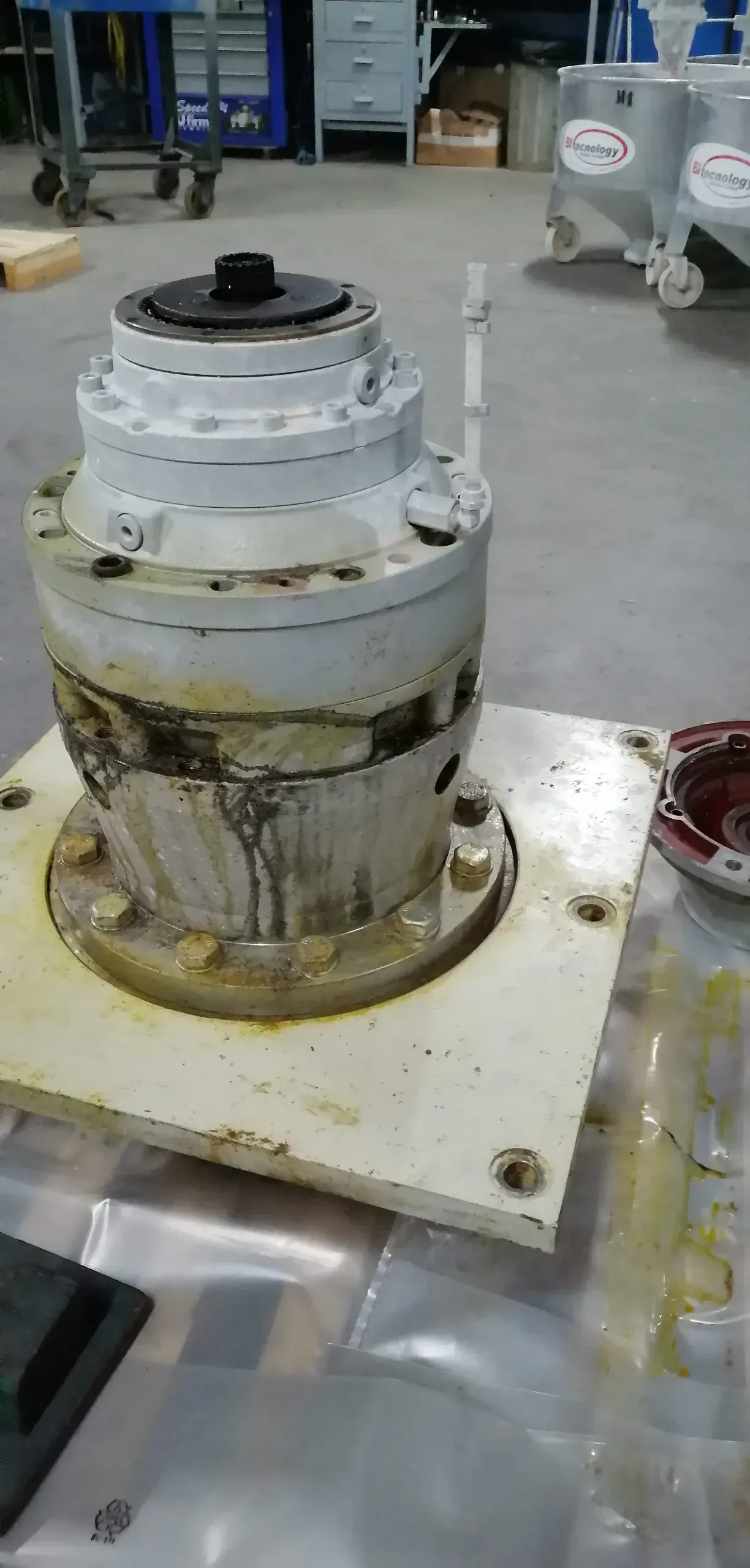 Un grande componente cilindrico di una macchina industriale, dipinto di bianco, è appoggiato su una base quadrata in un'officina.