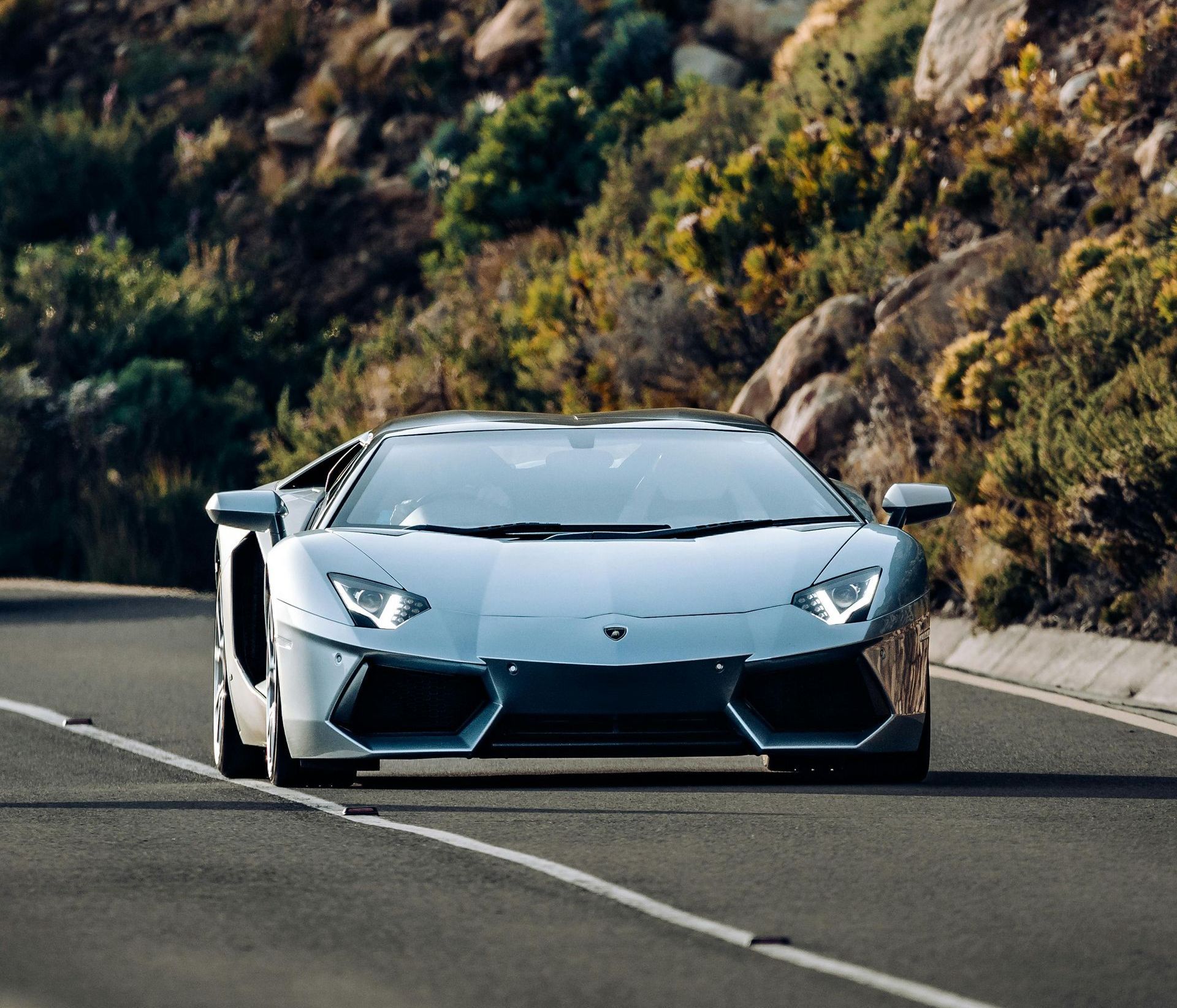 A Lamborghini aventador is driving down a mountain road.