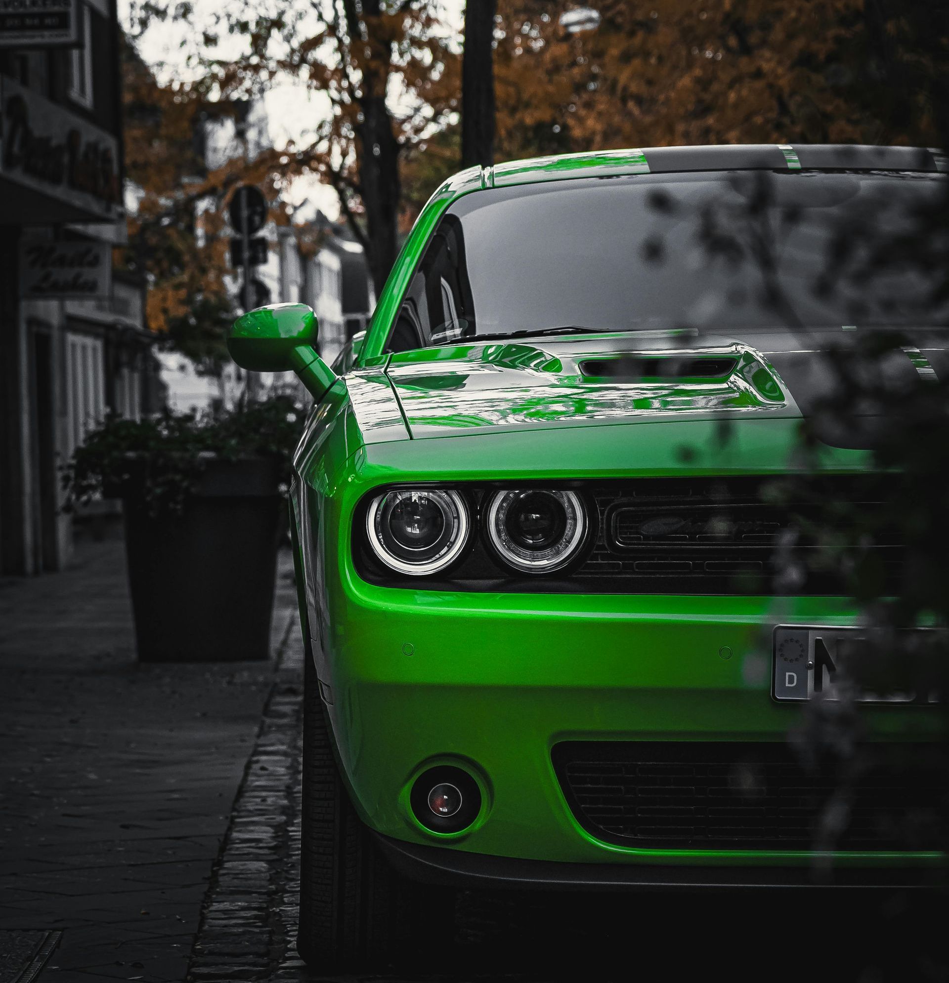 A green dodge challenger is parked on the side of the road.