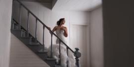 Bride in a white dress standing on a staircase in a bright room.