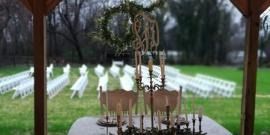 Outdoor wedding ceremony setup with white chairs facing a wooden arch under a pavilion.