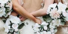 Hands clasped over a white floral wedding bouquet arrangement.