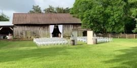 Rustic barn wedding setup with white chairs arranged on a green lawn