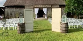 Outdoor wedding entrance with open doors, white chairs on grass, and a wooden barn backdrop