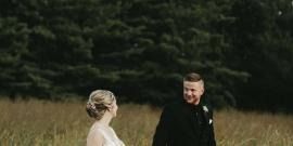 Two people standing in a field, facing each other with trees in the background.