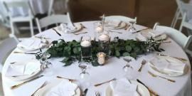 Round white dining table set with greenery centerpiece, candles, and neatly arranged plates and glasses