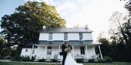 Couple standing in front of a white house with a porch and large trees