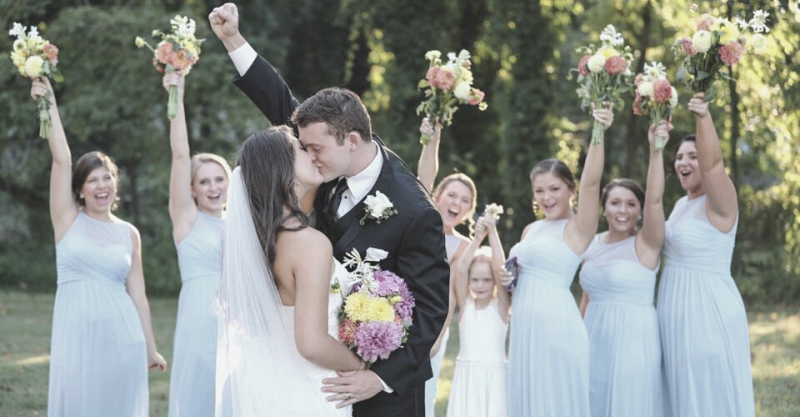 Wedding couple kissing with bridesmaids in light blue dresses holding bouquets outdoors