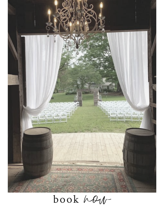 Elegant outdoor wedding aisle framed by white drapes, chandelier, and rows of white chairs facing a tree.