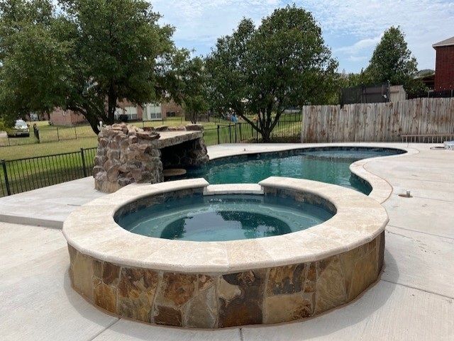 Pool with a spa, a waterfall feature, and surrounding concrete patio.