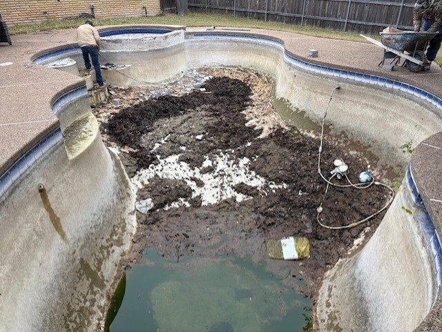 Pool being renovated; muddy bottom, workers, partially drained with green water, concrete surround.