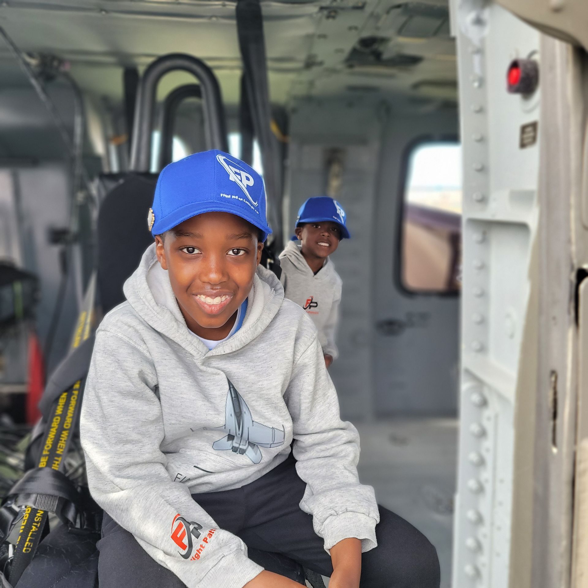 Jaxon Prear in a blue cap and gray hoodie sitting inside a helicopter, with another child in the back.