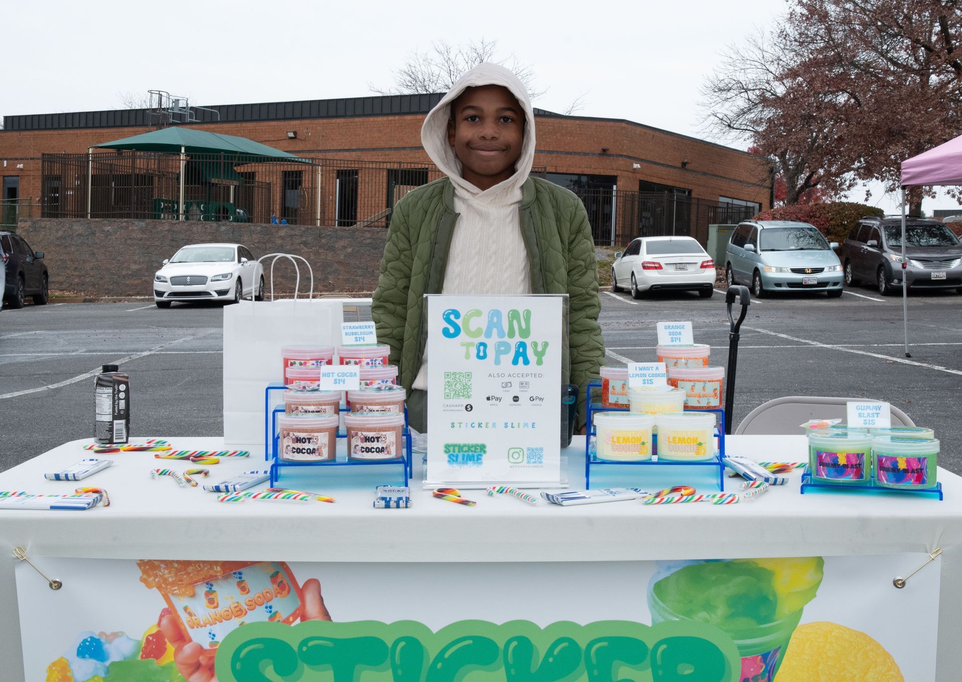 Person behind a table at a school-style food drive with boxes and a “Scan Today” sign outdoors