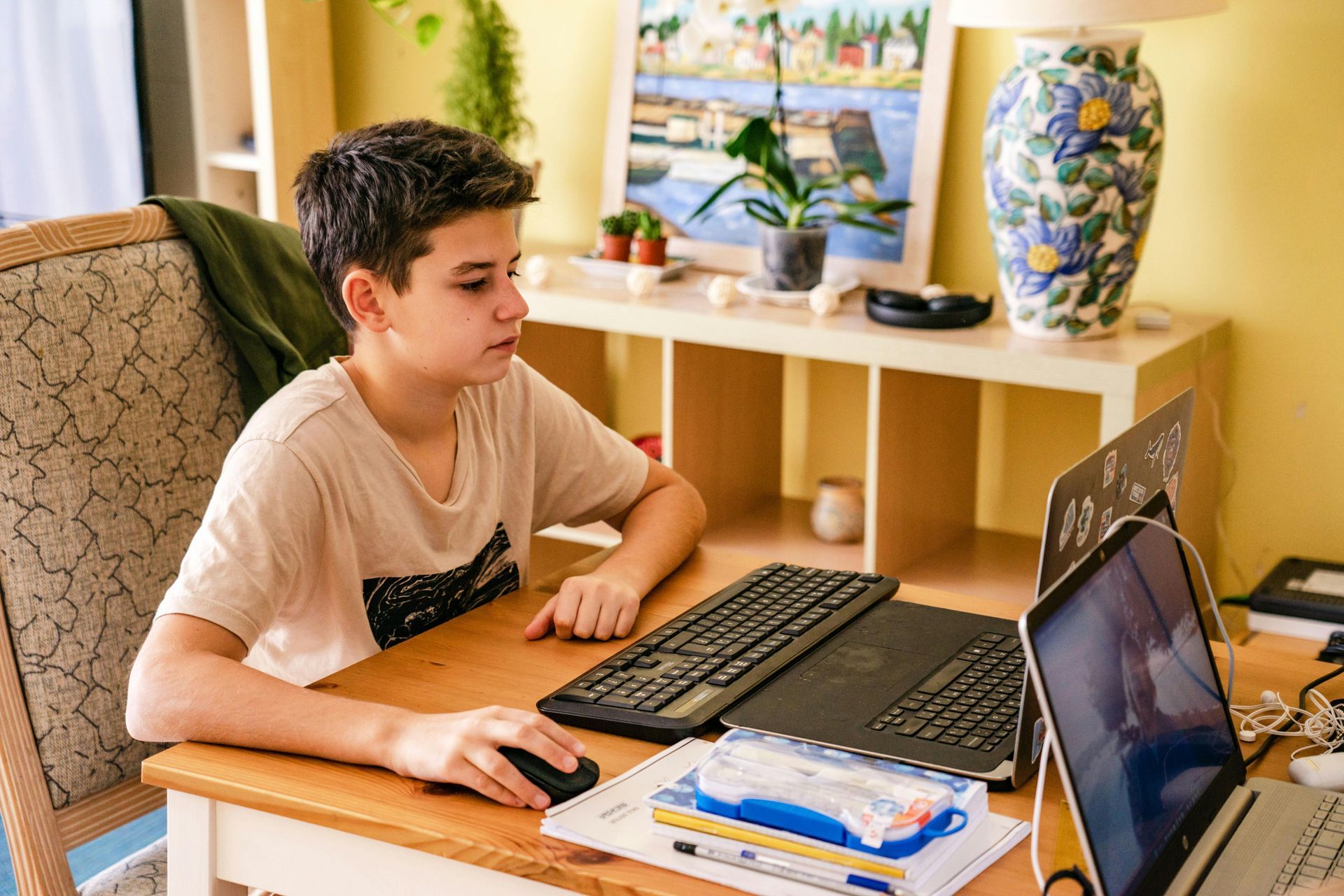 Kid Entrepreneur seated at a desk using a computer, with keyboard, laptop, and notebooks in a bright home office.