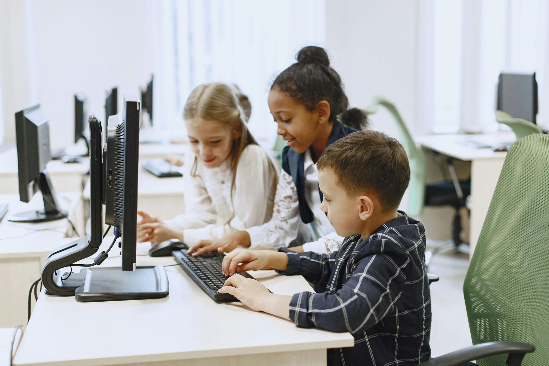 Three children using desktop computers together in a bright classroom