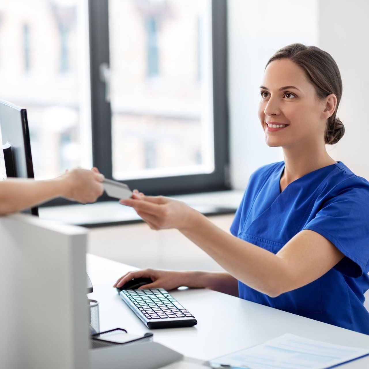 A woman in blue scrubs is giving a credit card to another woman